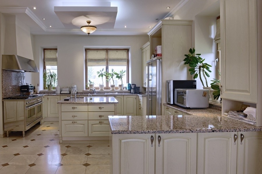 Photo of a white kitchen with beige countertops and recessed lighting in the ceiling over the island. 
